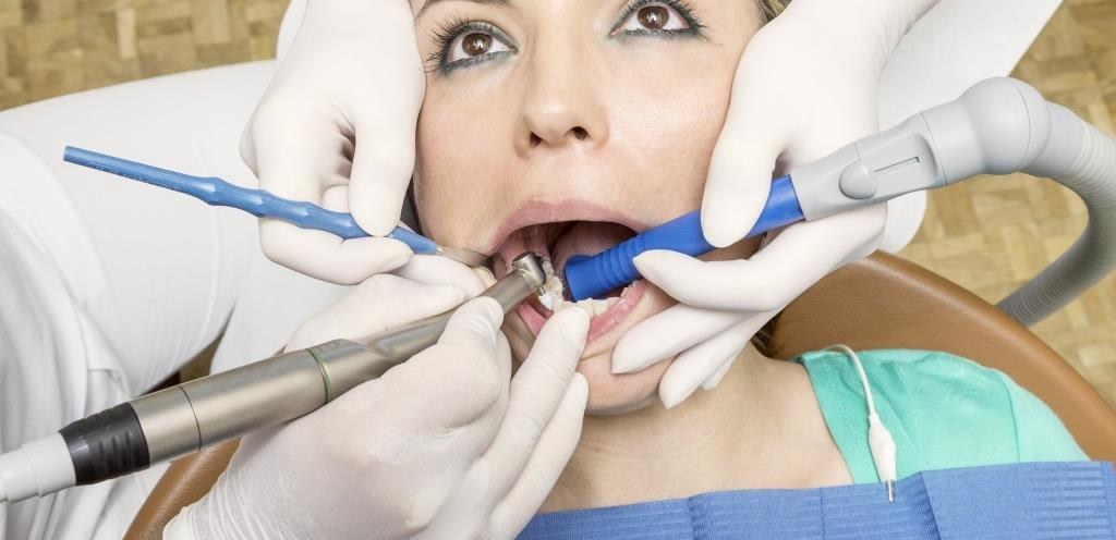 Assistante dentaire tenant la grosse canule d’aspiration près de l’instrument en travail à quatre mains